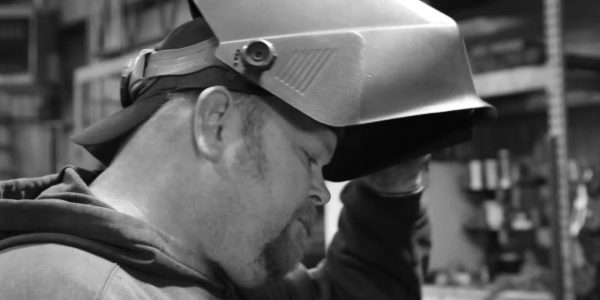 Man in welding mask, creating custom iron decor.